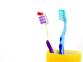 Two colorful toothbrushes in yellow mug isolated on white