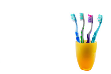 Four colorful toothbrushes in yellow mug isolated on white