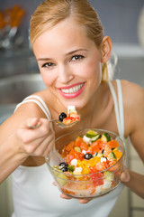 Portrait of young happy woman eating salad at kitchen