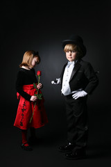 young boy in tux in foreground while girl in red looks at a rose