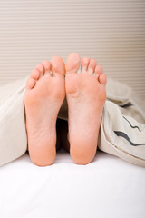woman's bare feet under duvet