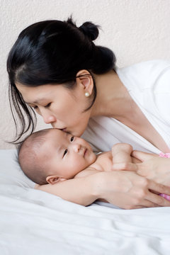 Mother and baby lying in bed, mother embracing and kissing baby