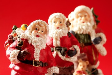 Three Santa Claus figurines over red background, studio