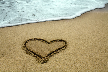 Fototapeta na wymiar handwritten heart on sand with wave approaching