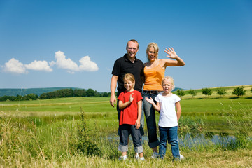 Familie auf der Wiese vor dem Teich winkt