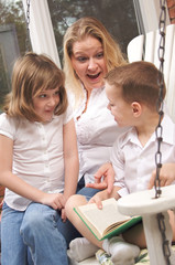 Fototapeta premium Young Boy Reads to His Mother and Sister