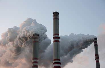 Three smoking chimneys in coal power plant against blue sky