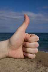thumb up on a blues sky, ocean and beach background