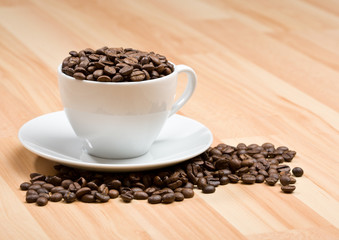 Cup with freshly roasted coffee beans on hardwood floor