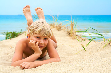 Young blond boy lying on the beach © Sergios