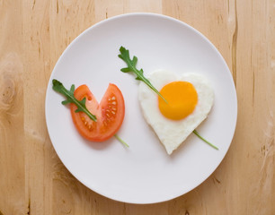 Fried egg and slice of tomato in the shape of two hearts