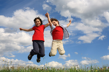 Kids running, jumping on green meadow against blue sky