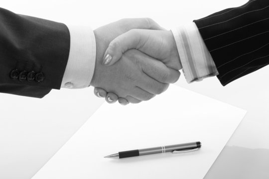 Business handshake over page with pen, b&w