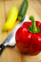 red bell pepper with knife and squash on cutting board