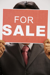 man holding a for sale signn cover the face