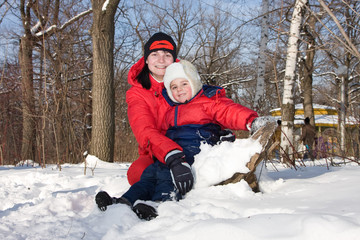 Mum with the son sit on snow in park
