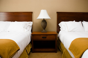 Table and lamp between two beds with white sheets.
