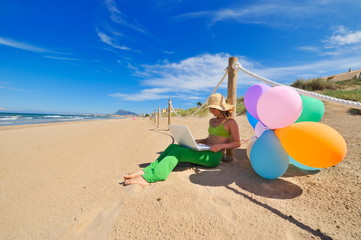 Fototapeta na wymiar young woman with colorful balloons using laptop on the beach
