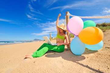 Fototapeta na wymiar young woman with colorful balloons using laptop on the beach