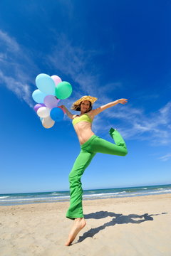 young woman with colorful balloons jumping on the beach
