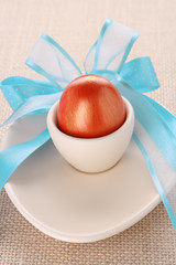 red golden easter egg in beige cup with blue bow