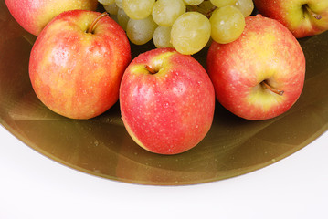 Red apples and green grapes on a plate. White background.