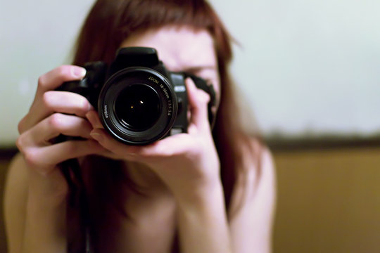 Jeune femme prenant une photo avec un reflex num&eacute;rique en mains