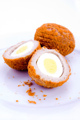 A halved scotch egg on plate on white