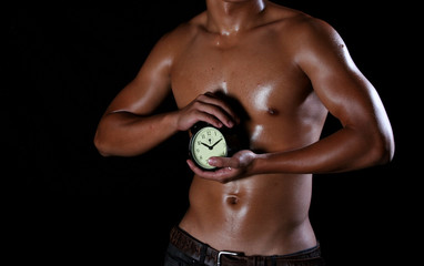 A hunky asian man holding a clock in his hands,