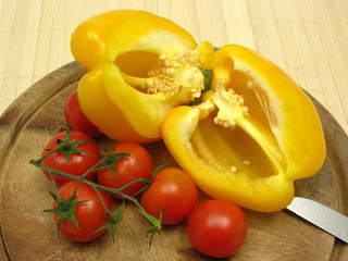 Halbierte gelbe Paprika und Tomaten auf Holzteller mit Messer