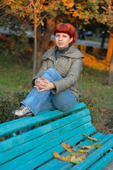 Autumn. Young girl with red hairs seating on bench.