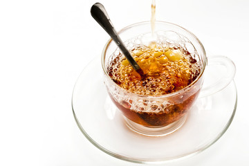 Pouring tea into a clear glass style cup on white background