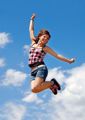 Fototapeta na wymiar Cute happy girl jumping under a blue sky