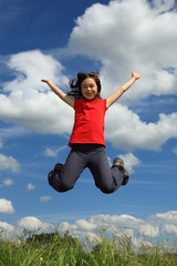 Kid running, jumping on green meadow against blue sky