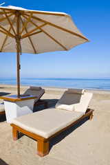 Deck chairs on the beach under an umbrella.