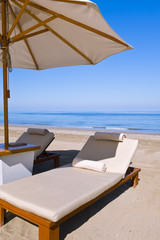 Deck chairs on the beach under an umbrella.