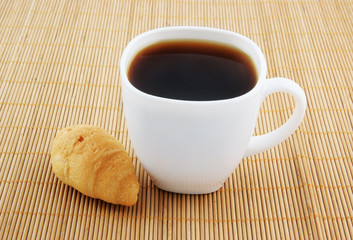 Small croissant and white cup of coffee for breakfast