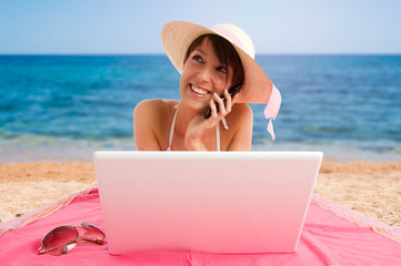 Girl using laptop at the beach, working and mobile speaking