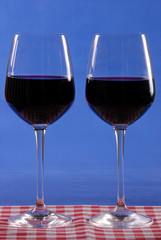 Two glasses of red wine. Glasses with stem. Red and white checkered tablecloth. Blue background. Vertical photo.