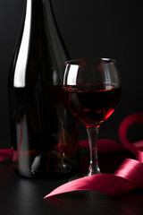 glass of red wine and red ribbon over black background