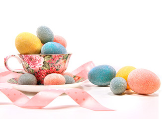 Brightly colored eggs in tea cup on white