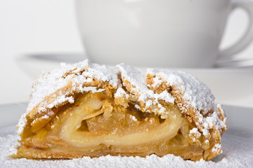 Apfelstrudel mit Puderzucker und einer Tasse im Hintergrund