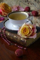 Teetasse auf altem Buch mit Rosen und Rosenkranz