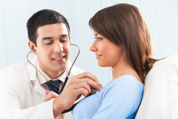 Doctor with stethoscope and female patient on bed at clinic