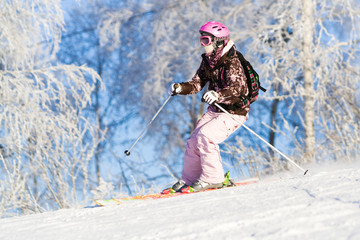 Girl riding on skis with white frozen trees on the background