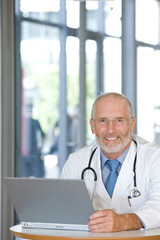 Portrait of a  senior caring doctor working on laptop