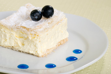 custard cake square on a plate with fresh blueberries