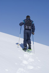 Man climbing a moutain with snowshoes.