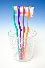 Coloured tooth brushes in a cup on a blue studio background.