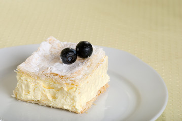 custard cake square on a plate with fresh blueberries